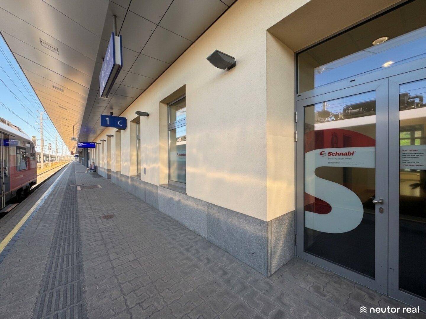 Außenansicht eines Gebäudes am Bahnsteig mit großen Fenstern und einer Glastür.