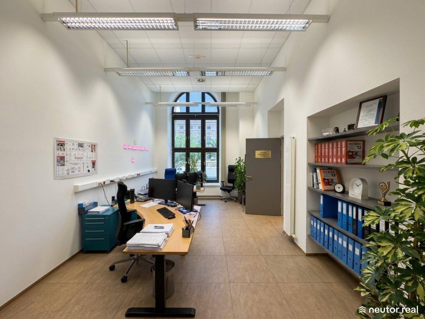 Langes Büro mit mehreren Arbeitsplätzen, Regalen und einem großen Fenster am Ende des Raumes.
