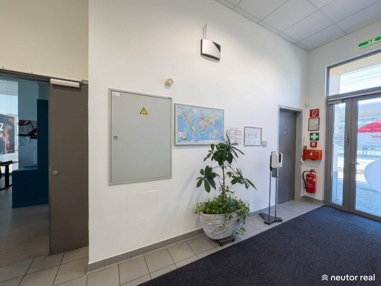 Eingangsbereich mit Fliesenboden, Sicherheitstafel und einer Pflanze, führt zu weiteren Räumen.