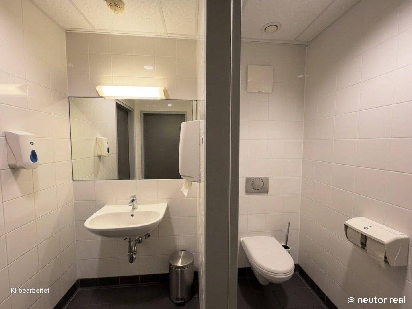 Saubere Toilette mit Waschbecken, Spiegel und weißen Fliesen an den Wänden.