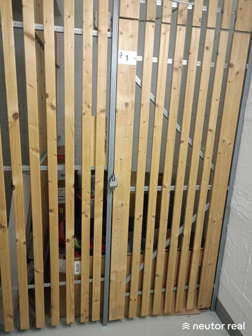 Abstellraum im Keller mit Holzlattenverschlag und Vorhängeschloss für persönliche Gegenstände.