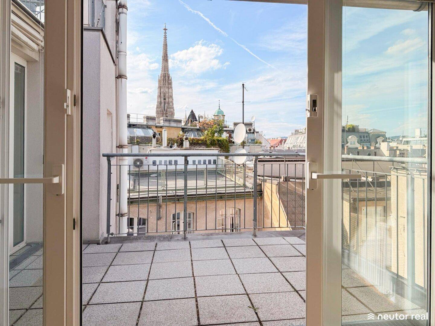 Geräumige Terrasse mit Fliesenboden und weitem Blick über die Dächer der Stadt mit Kirchturm.