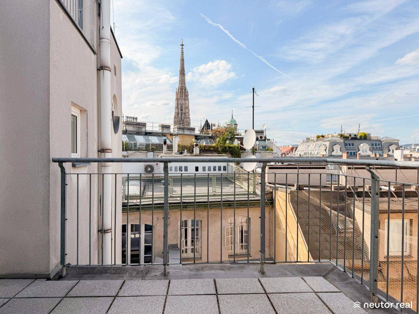 Helle Dachterrasse mit Metallgeländer und beeindruckendem Stadtpanorama inklusive Kirchturm.