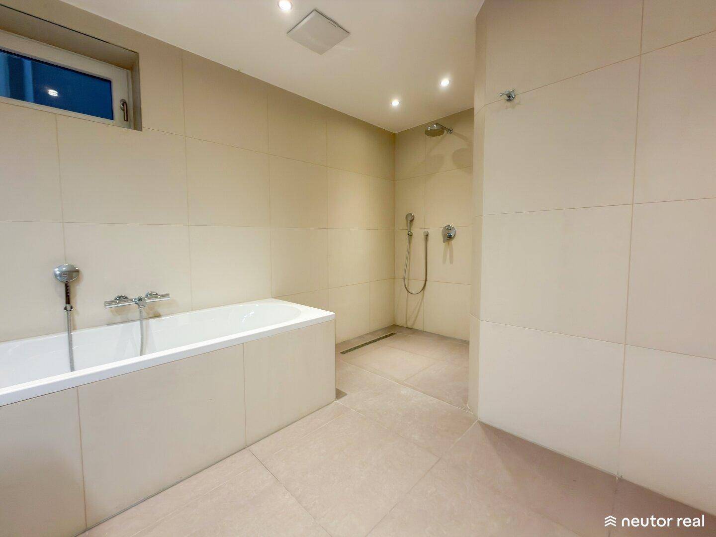 Geräumiges Badezimmer mit Badewanne und begehbarer Dusche, in hellen Fliesen gehalten.