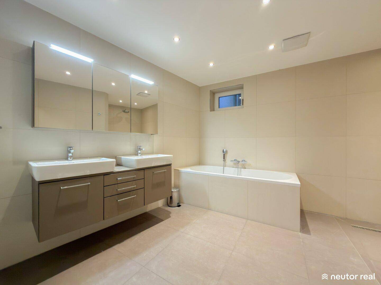 Modernes Badezimmer mit Doppelwaschbecken, Badewanne und großformatigen Fliesen in neutralen Tönen.