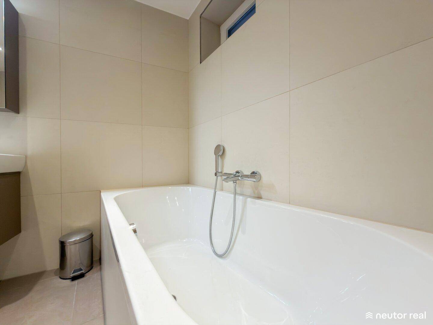 Modernes Badezimmer mit Badewanne und hellen Fliesen, ausgestattet mit einer Handbrause.