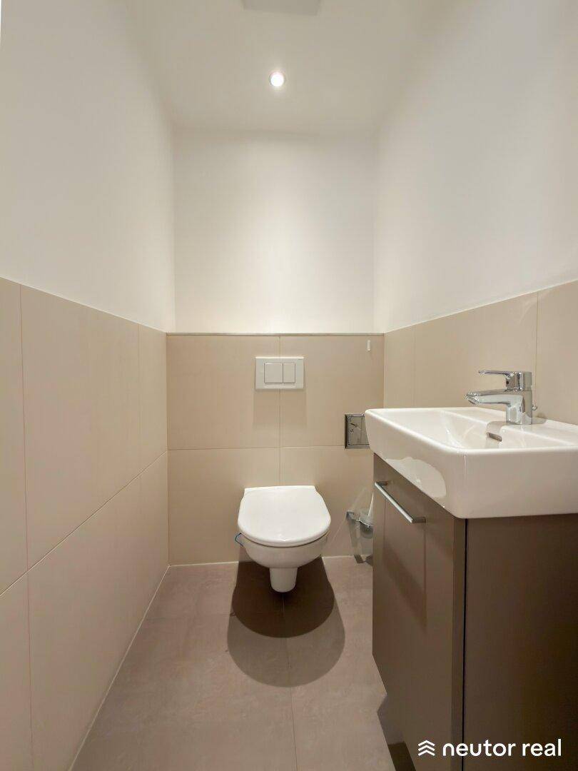 Modernes Gäste-WC mit wandhängender Toilette und kleinem Waschbecken, in neutralen Farben gehalten.