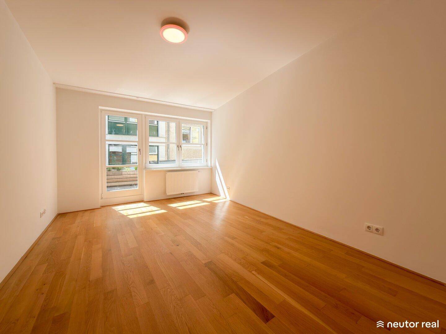 Helles Zimmer mit Holzboden und Zugang zu einem Außenbereich, ideal als Schlaf- oder Arbeitszimmer.