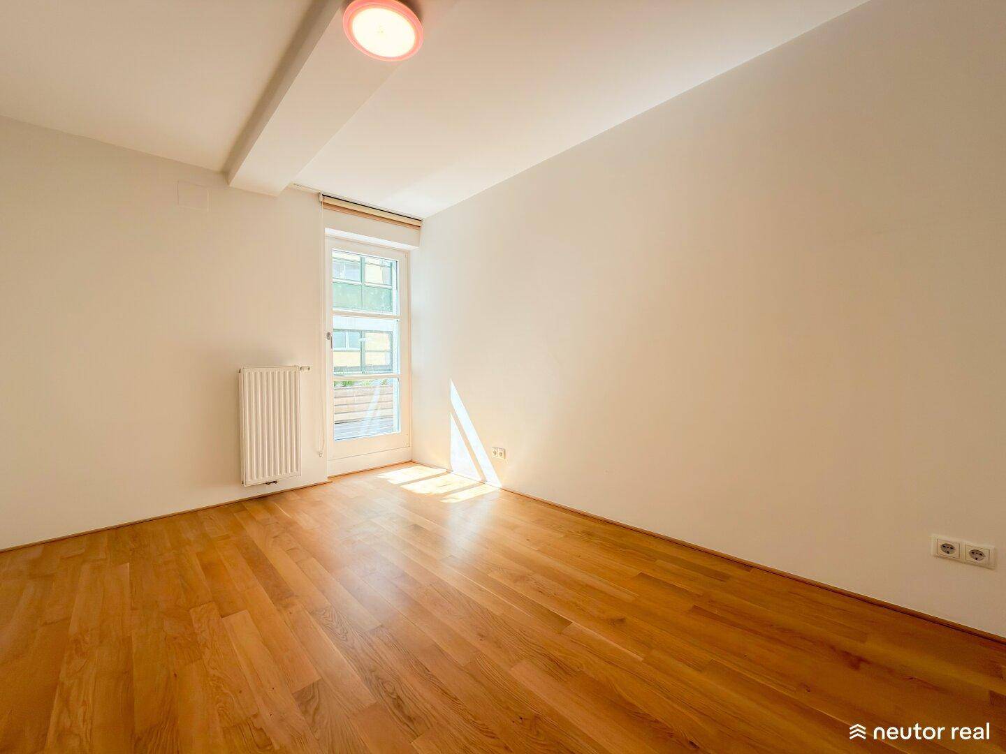 Lichtdurchflutetes Zimmer mit Holzboden und direktem Zugang zu einem sonnigen Außenbereich.