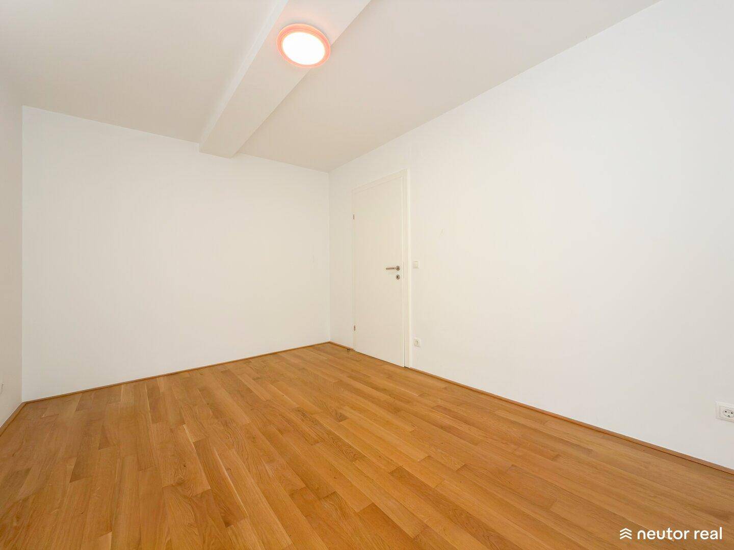 Schlichtes, helles Zimmer mit Holzboden und weiß gestrichenen Wänden, bereit zum Einrichten.