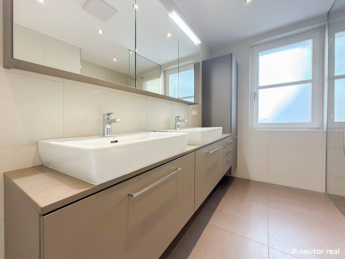 Helles Badezimmer mit Doppelwaschbecken, großem Spiegelschrank und Fenster für viel Licht.