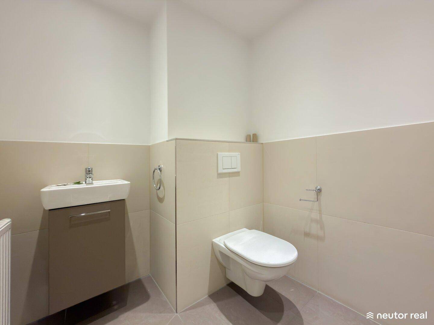 Praktisches Gäste-WC mit wandhängender Toilette und kleinem Waschbecken in hellen Fliesen.