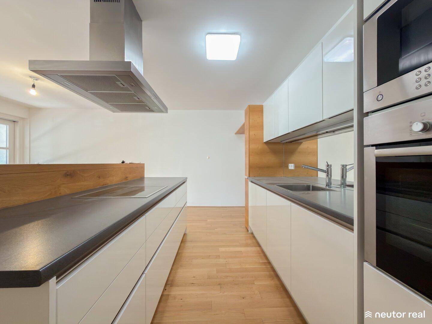 Elegante Küche mit minimalistischem Design, weißen Schränken und warmen Holzelementen für eine gemütliche Atmosphäre.