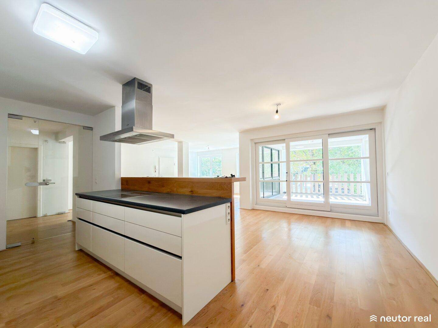 Offener Küchenbereich mit Kochinsel und direktem Zugang zum hellen Wohnzimmer und Balkon.