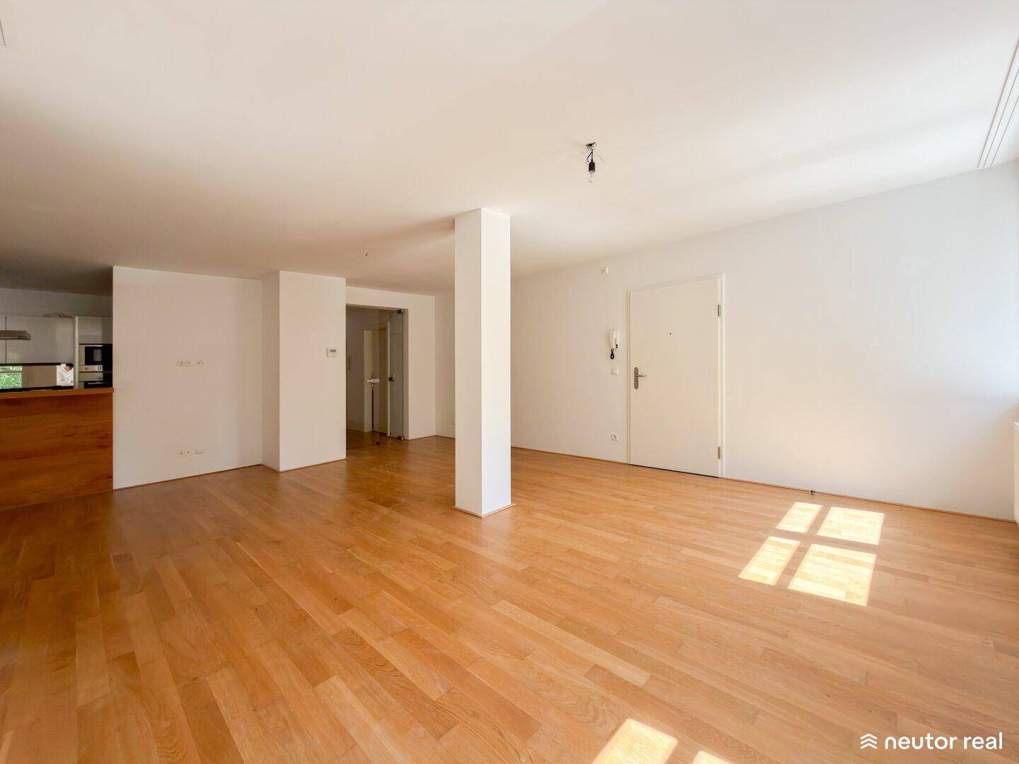 Geräumiger, heller Wohnbereich mit Holzboden und offener Verbindung zur Küche und Eingangstür.