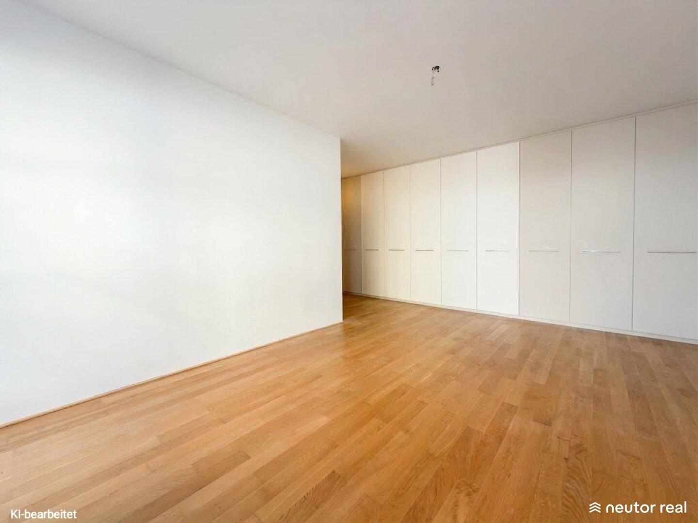 Geräumiges Zimmer mit Holzboden und einer langen Wand aus integrierten, weißen Kleiderschränken.