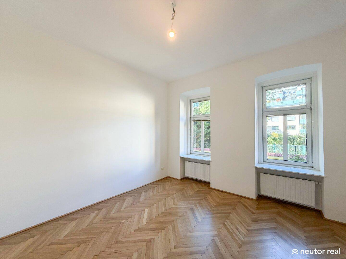 Helles Zimmer mit Fischgrätparkett und zwei Fenstern, ideal als Wohn- oder Schlafzimmer.