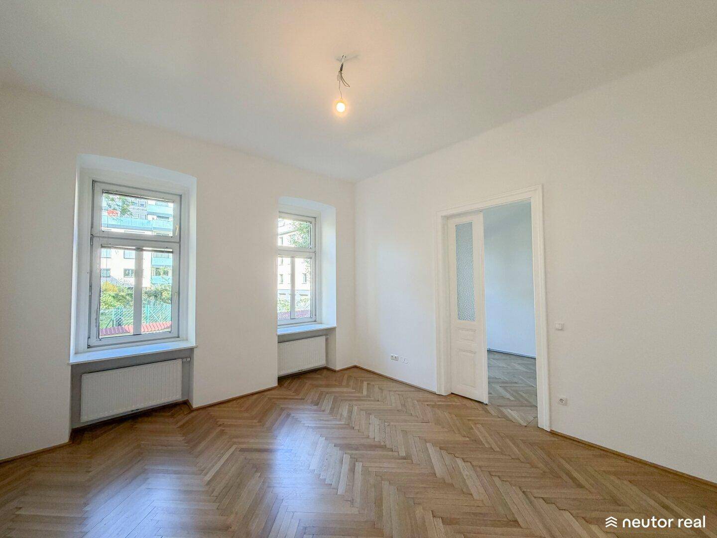 Geräumiges Zimmer mit Fischgrätparkett und Zugang zu einem weiteren Raum, hell und einladend.