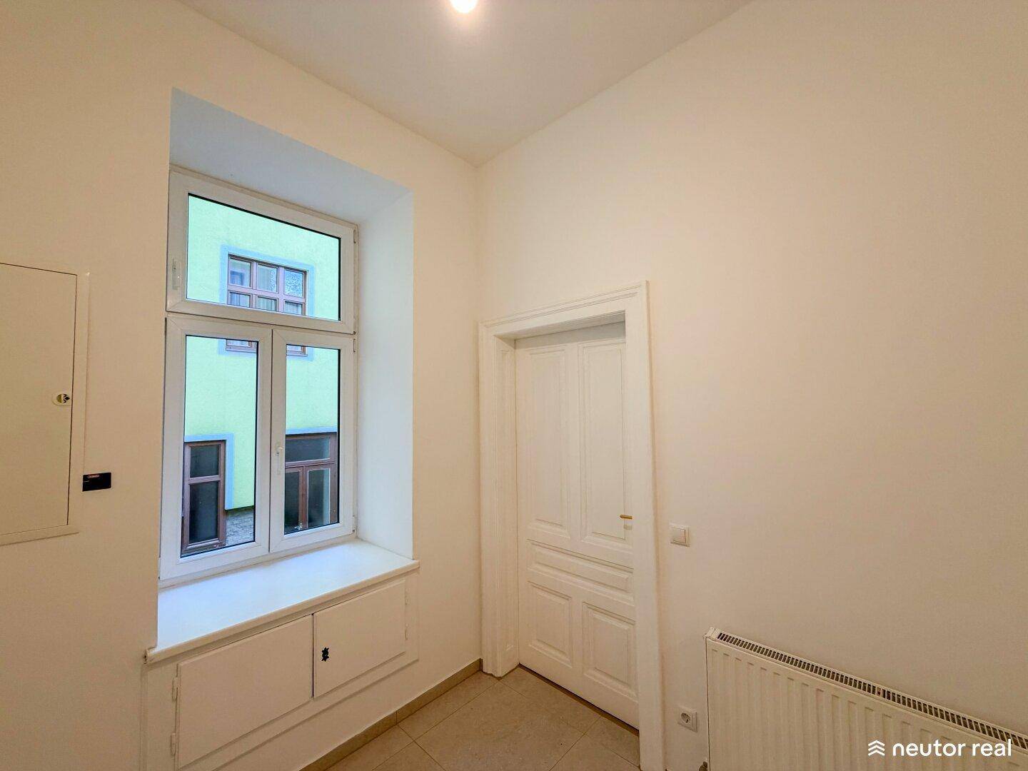 Heller Flur mit Fliesenboden, Fenster mit Einbauschrank und einer charmanten Holztür.