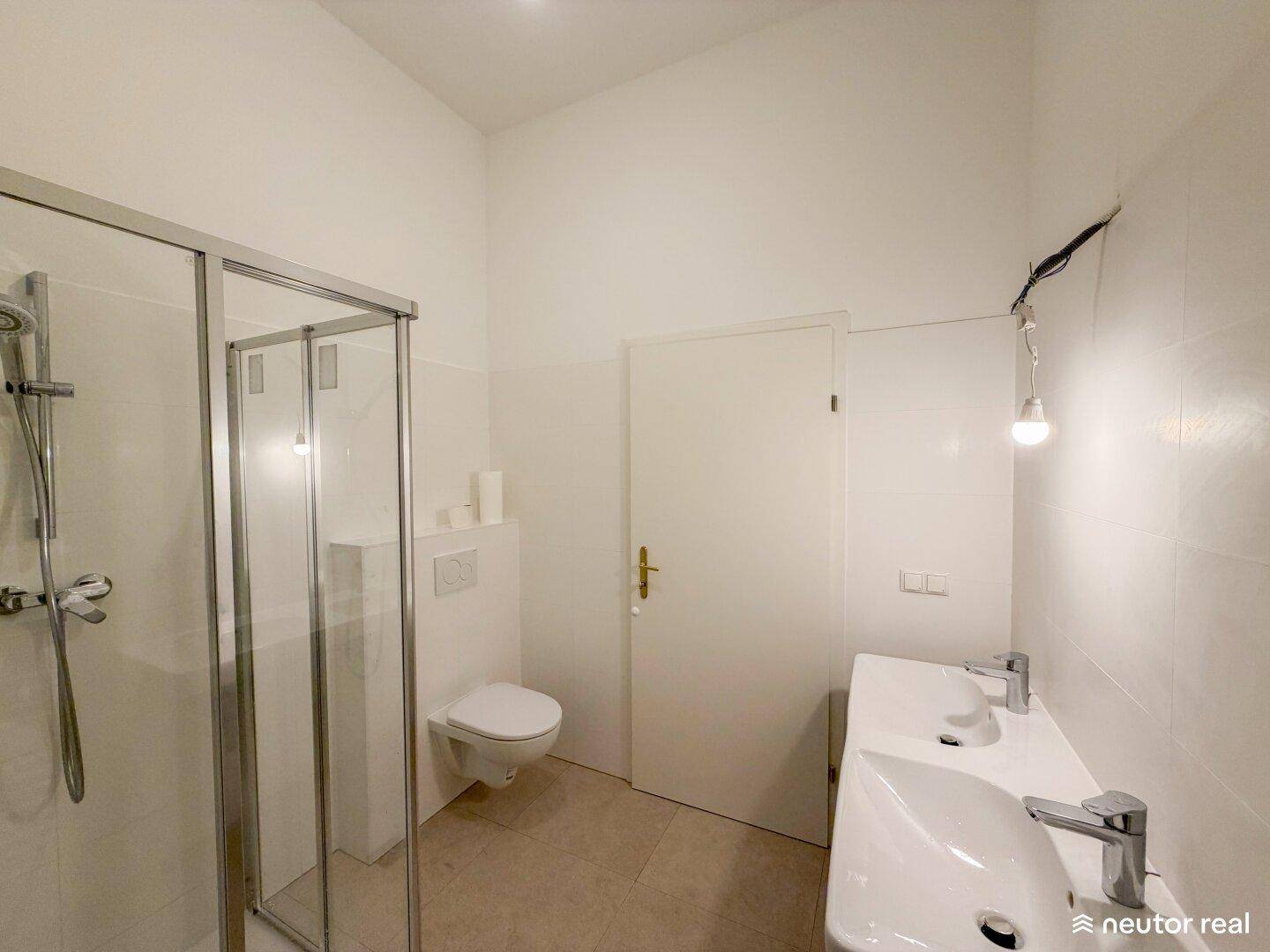 Modernes Badezimmer mit Duschkabine, Doppelwaschbecken und wandhängendem WC, hell gefliest.
