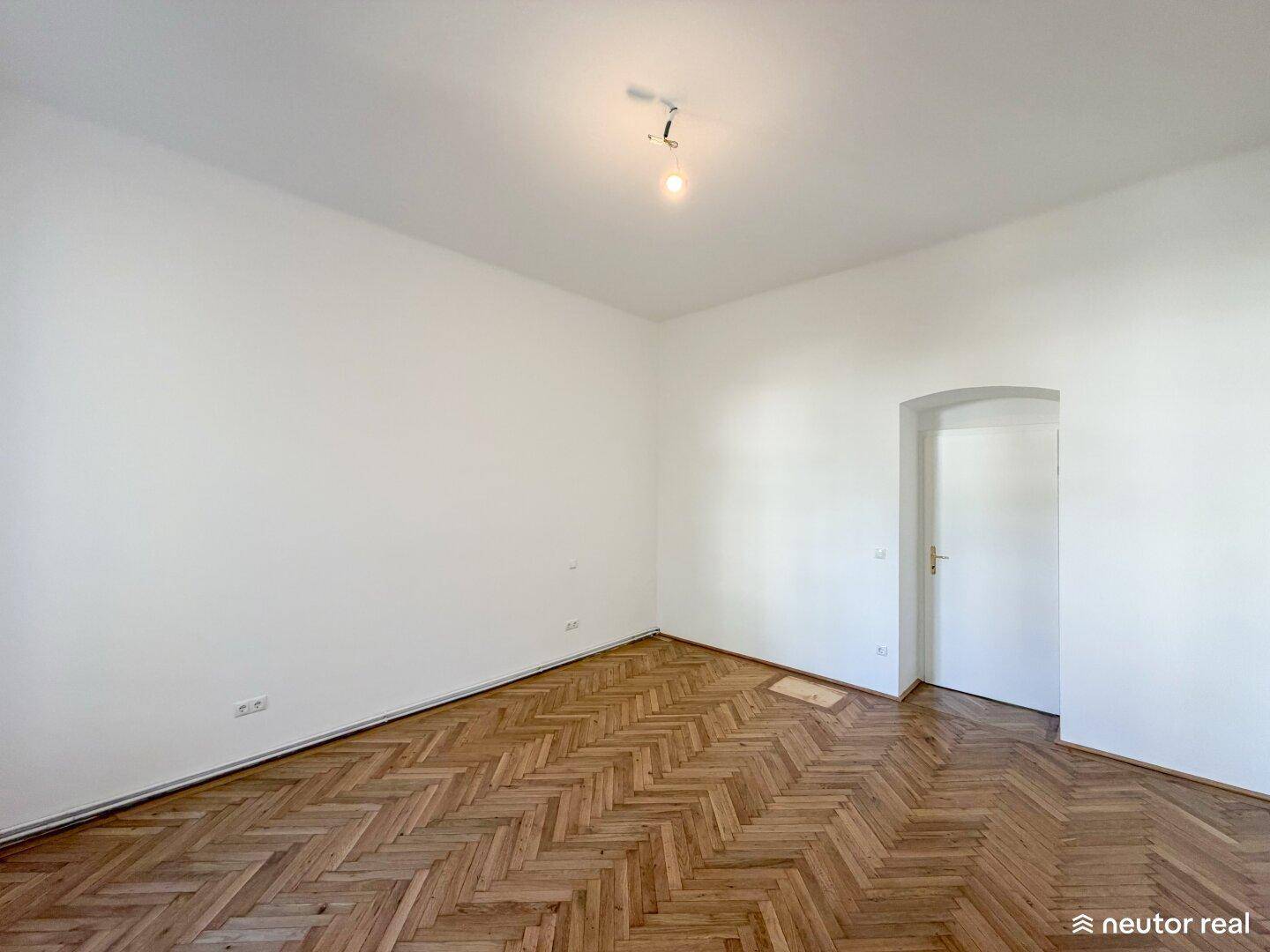 Geräumiges Zimmer mit Fischgrätparkett und einem eleganten Rundbogen, vielseitig nutzbar.