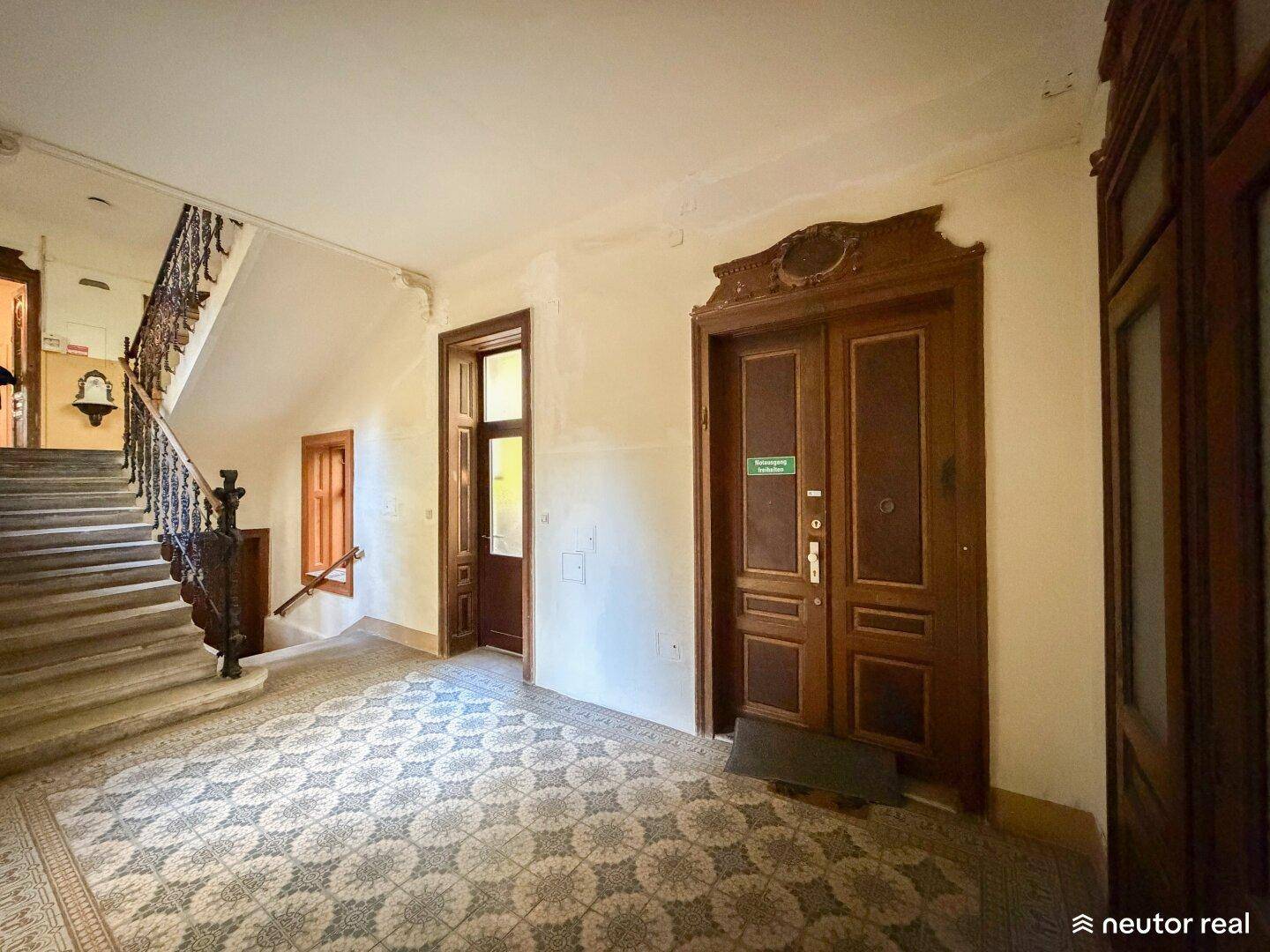 Repräsentativer Eingangsbereich eines Altbaus mit prächtiger Treppe, gemustertem Fliesenboden und Holztüren.