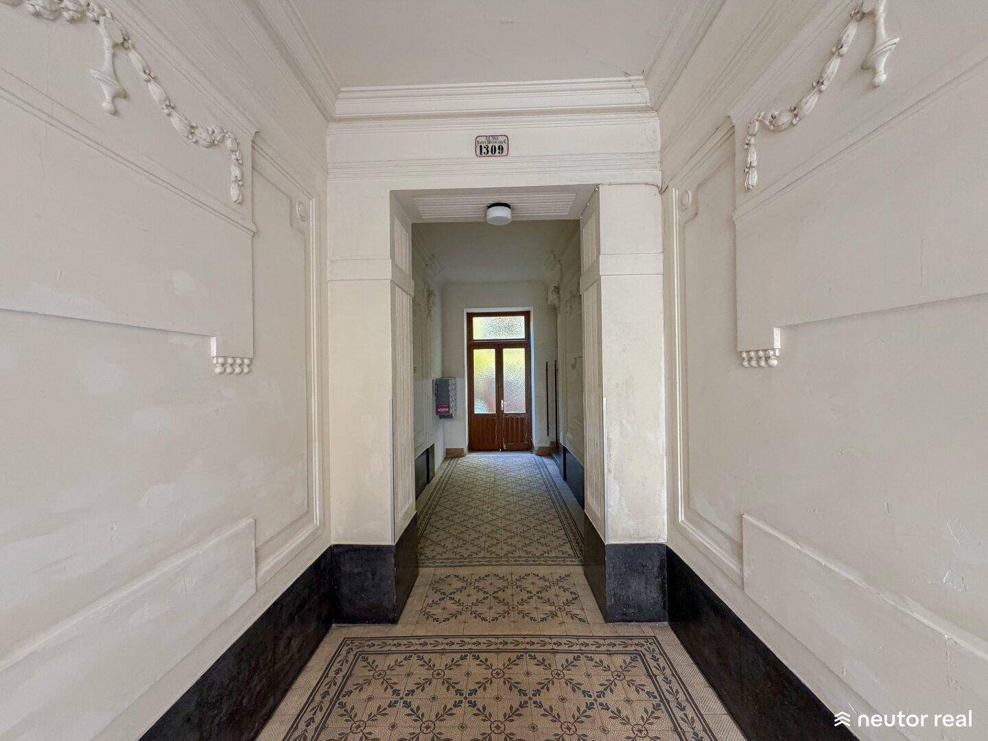 Langer Flur in einem Altbau mit gemustertem Fliesenboden und dekorativen Wandelementen.
