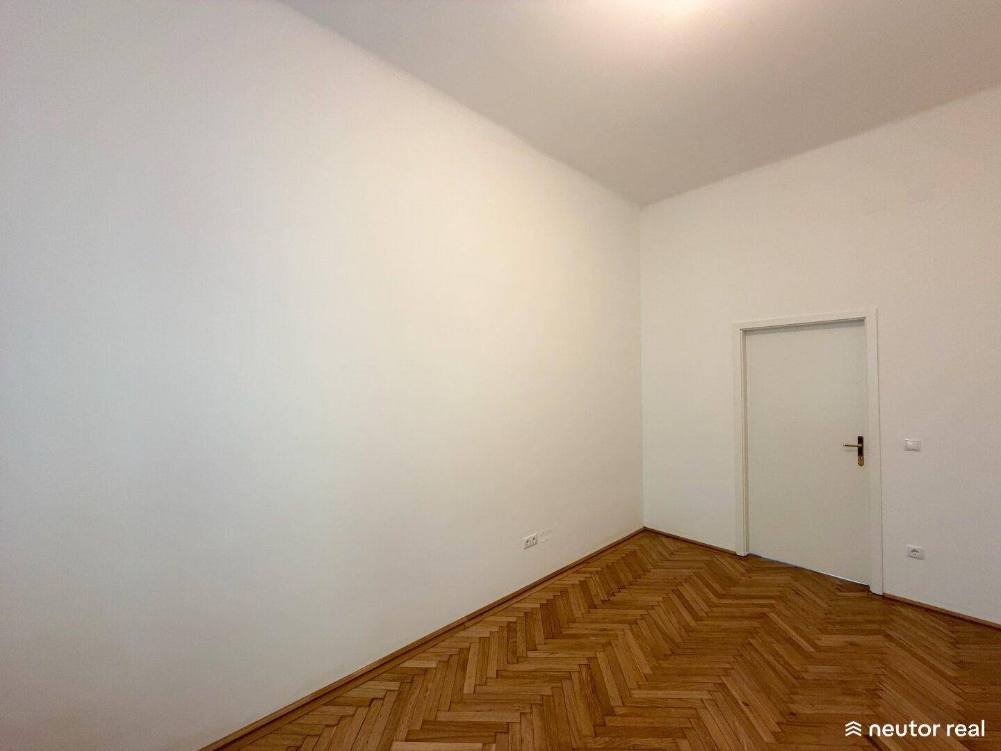 Schlichtes Zimmer mit Fischgrätparkett und weißer Tür, bereit zur individuellen Gestaltung.