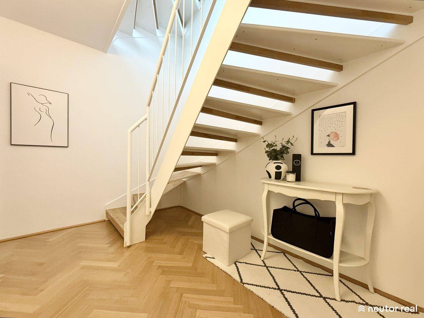 Heller Flur mit offener Holztreppe, Fischgrätparkett und moderner Einrichtung.