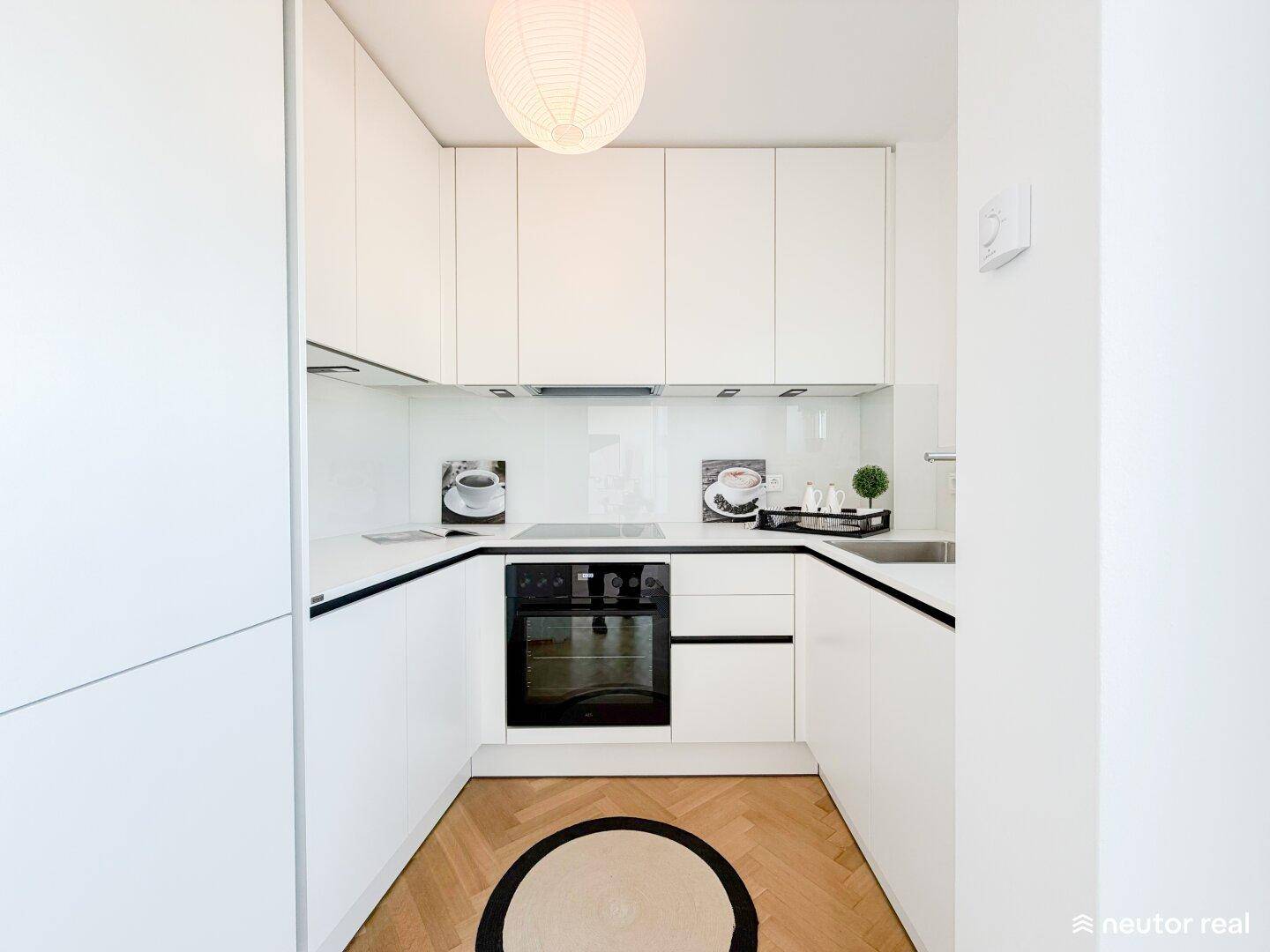 Moderne, kompakte Küche mit weißen Hochglanzfronten, integriertem Backofen und Parkettboden.