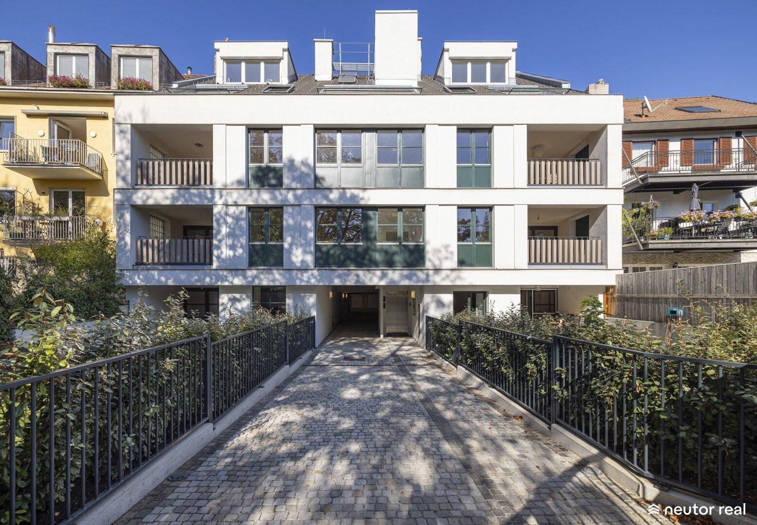 Moderne Wohnhausfassade mit Balkonen und Zufahrt zur Tiefgarage unter blauem Himmel.