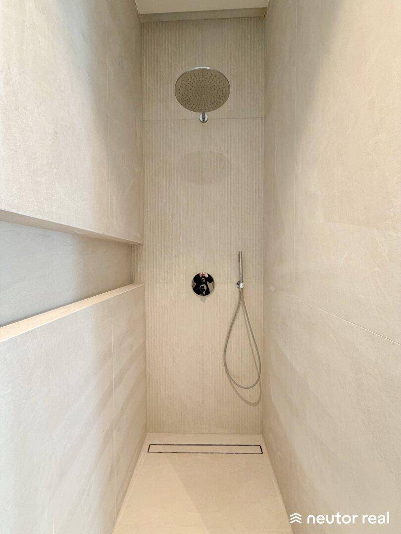 Elegante begehbare Dusche mit Regenduschkopf und modernen Fliesen in hellem Farbton.