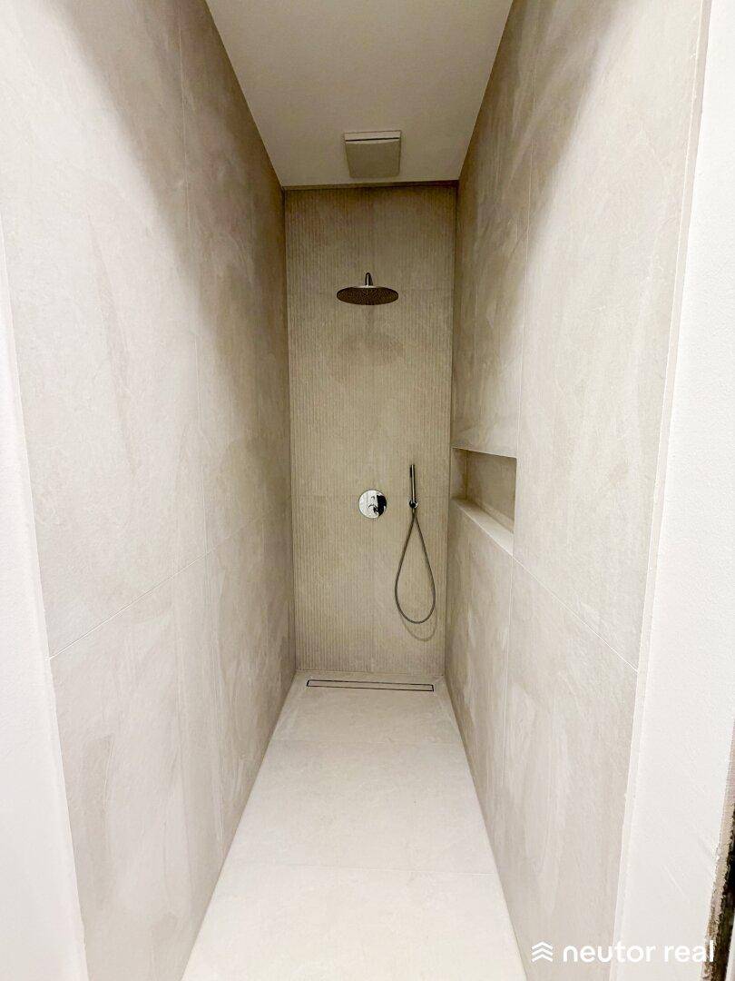 Elegante begehbare Dusche mit Regenduschkopf und modernen, hellen Fliesen.
