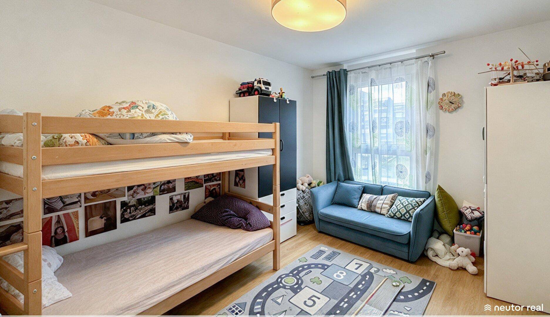 Kinderzimmer mit Etagenbett, blauem Sofa und Spielteppich, bietet Platz zum Schlafen und Spielen.