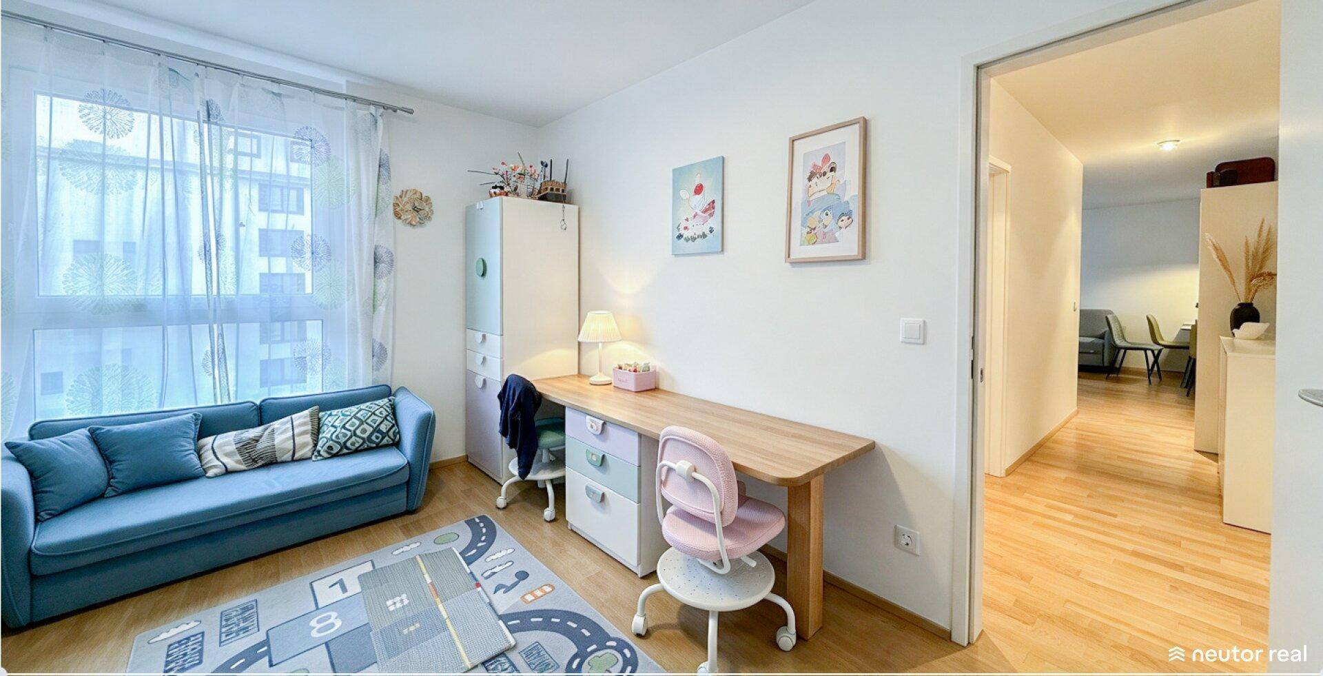 Helles Kinderzimmer mit Schreibtisch, blauem Sofa und großem Fenster, ideal zum Lernen und Entspannen.