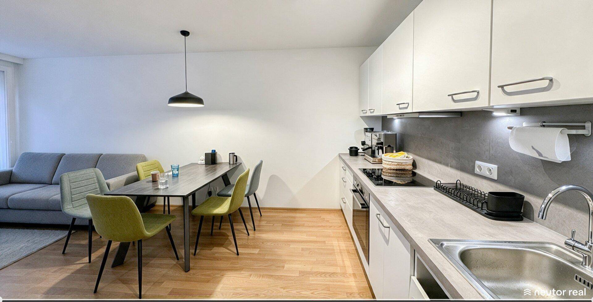 Offener Wohnbereich mit integrierter Küche, Esstisch und Sofa, ideal für geselliges Beisammensein.