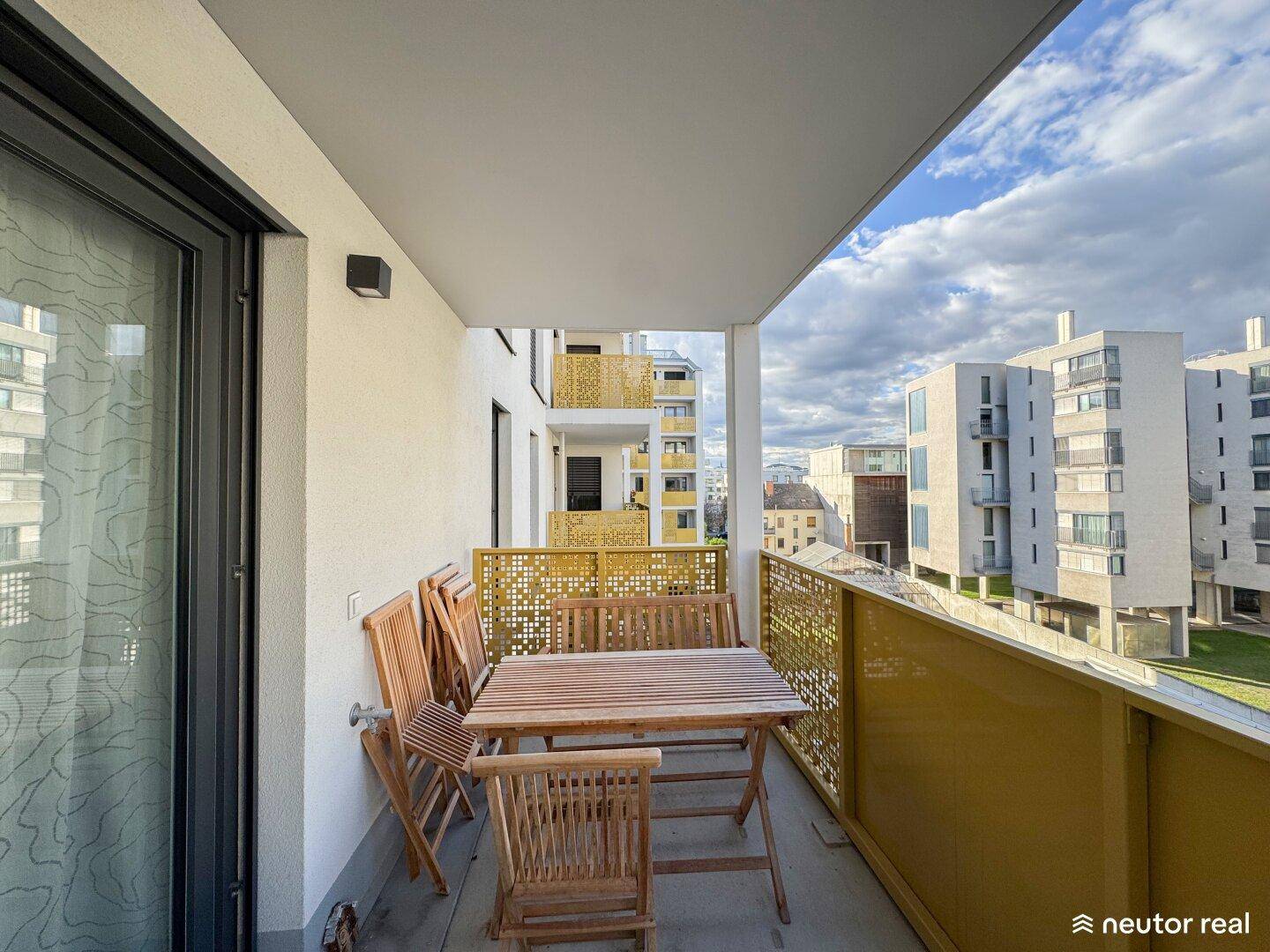 Geräumiger Balkon mit Holzmöbeln und Blick auf die umliegenden modernen Wohngebäude.