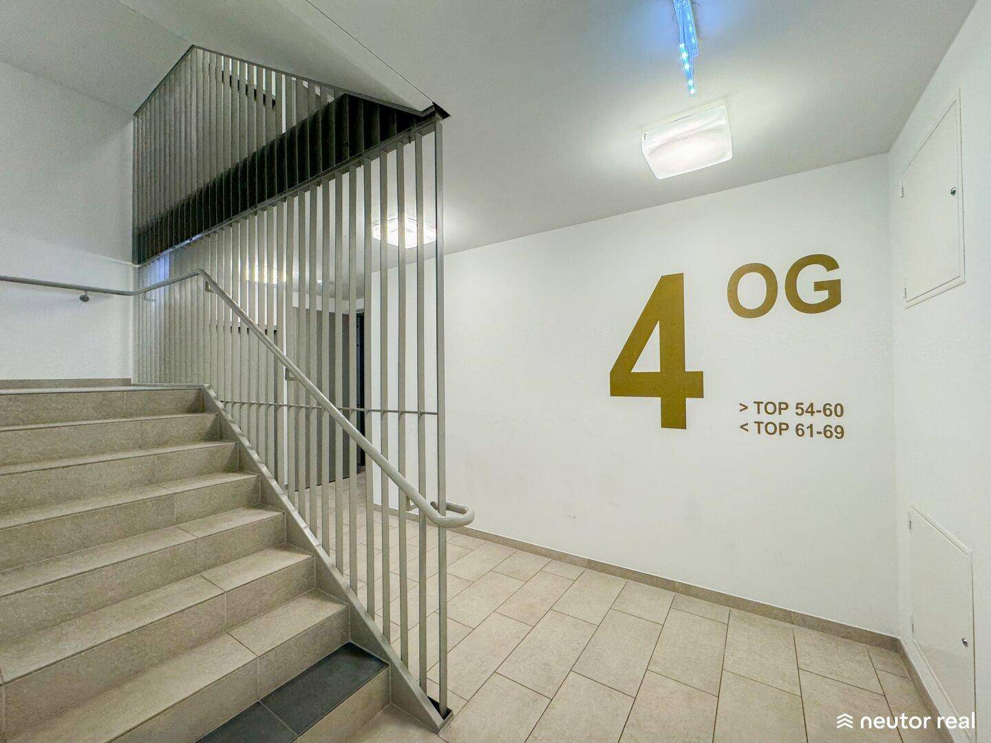 Helles Treppenhaus im modernen Gebäude, führt zum vierten Obergeschoss mit Wohnungsnummern.