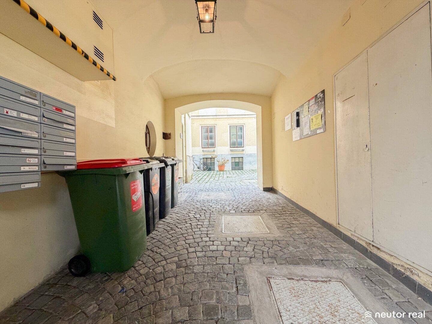 Eingangsbereich mit Torbogen, Briefkästen und Blick auf den Innenhof mit Kopfsteinpflaster.