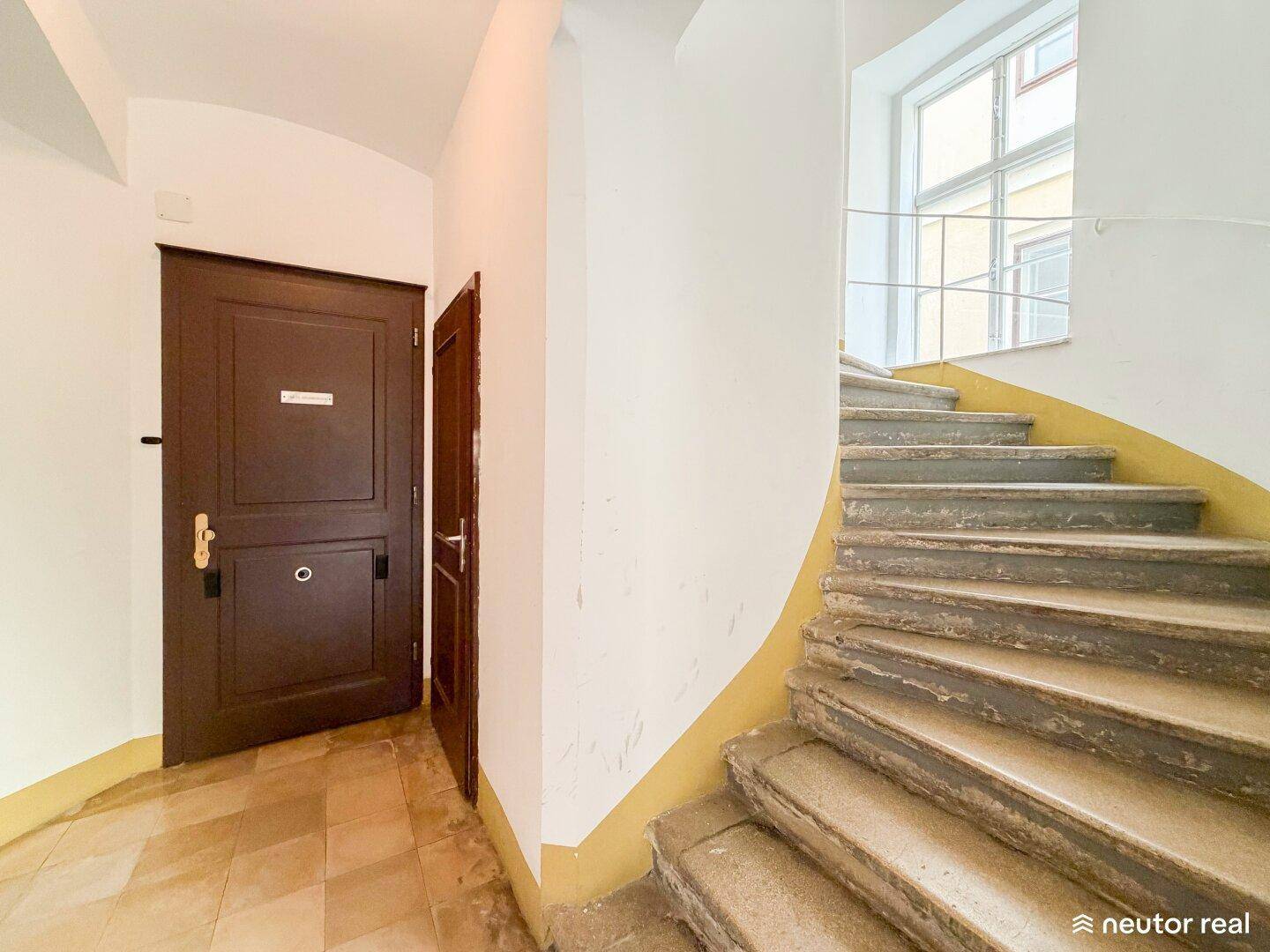 Historisches Treppenhaus mit Steinstufen und einem Fenster, das Licht in den Eingangsbereich bringt.
