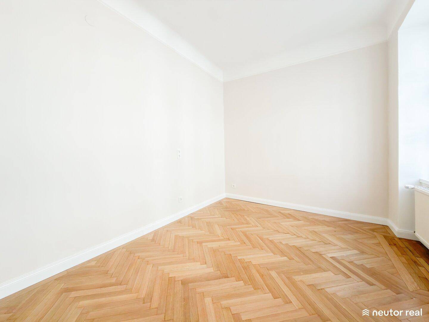 Leeres Zimmer mit hellem Fischgrätparkett und weiß gestrichenen Wänden, bereit zur Einrichtung.