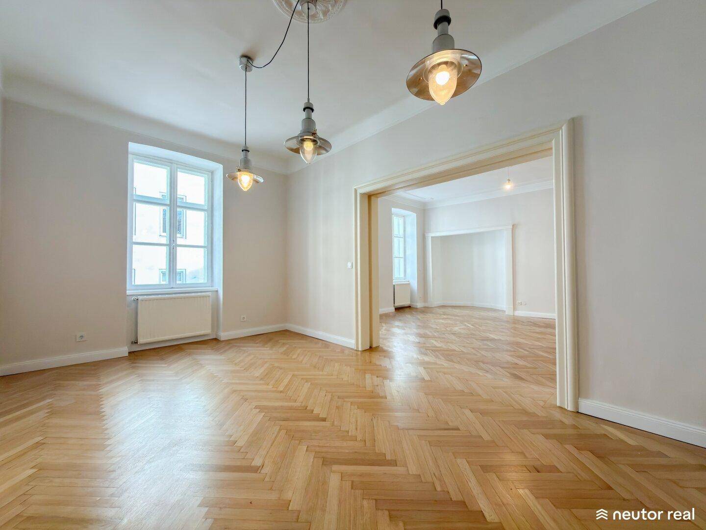 Helles Wohnzimmer mit Fischgrätparkett, hohen Decken und modernen Hängelampen.