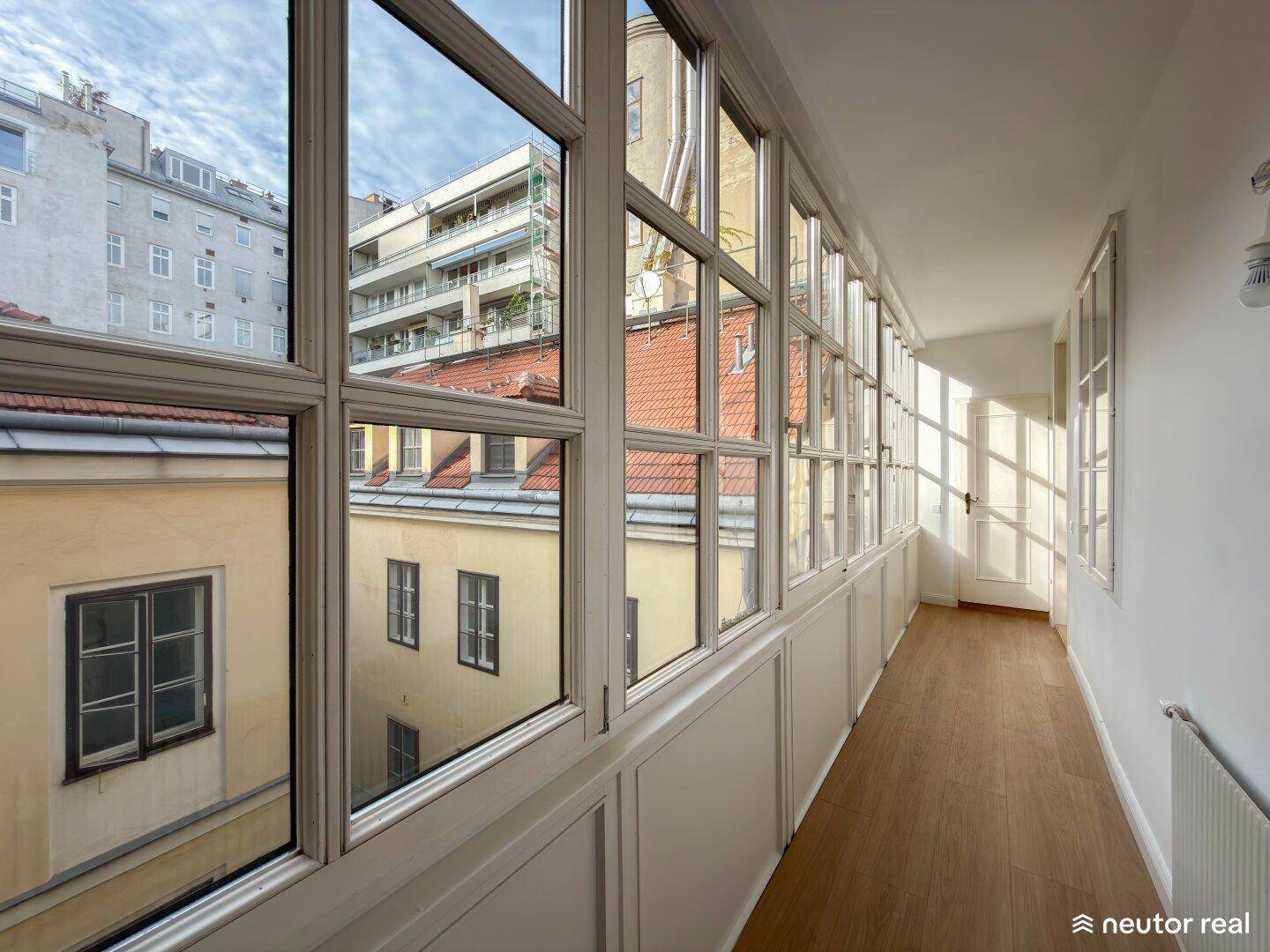 Heller Wintergarten mit vielen Fenstern und Blick auf die umliegenden Gebäude und Dächer.