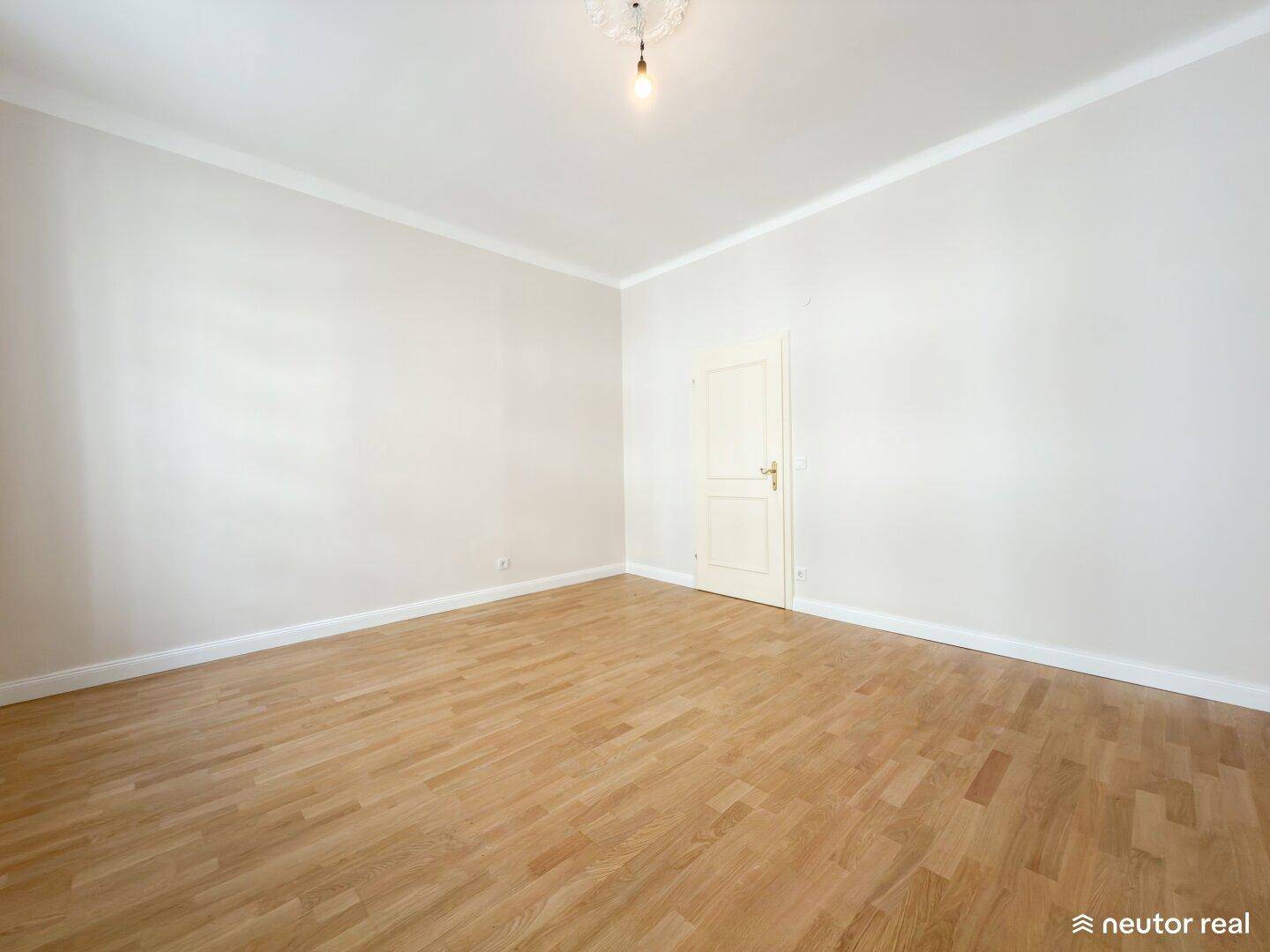 Leeres Zimmer mit Fischgrätparkett, hohen Decken und einer schlichten Tür, bereit zur Gestaltung.