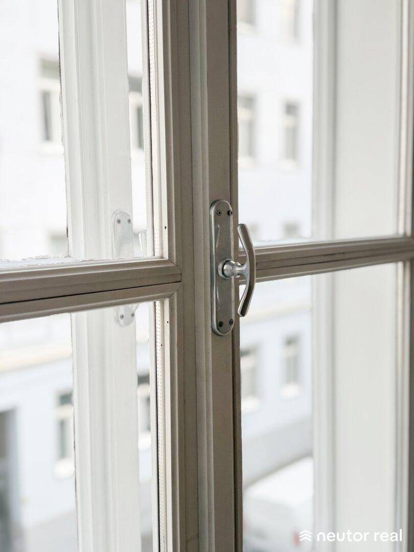 Nahaufnahme eines Fensters mit Sprossen und einem klassischen Fenstergriff, Blick nach draußen.
