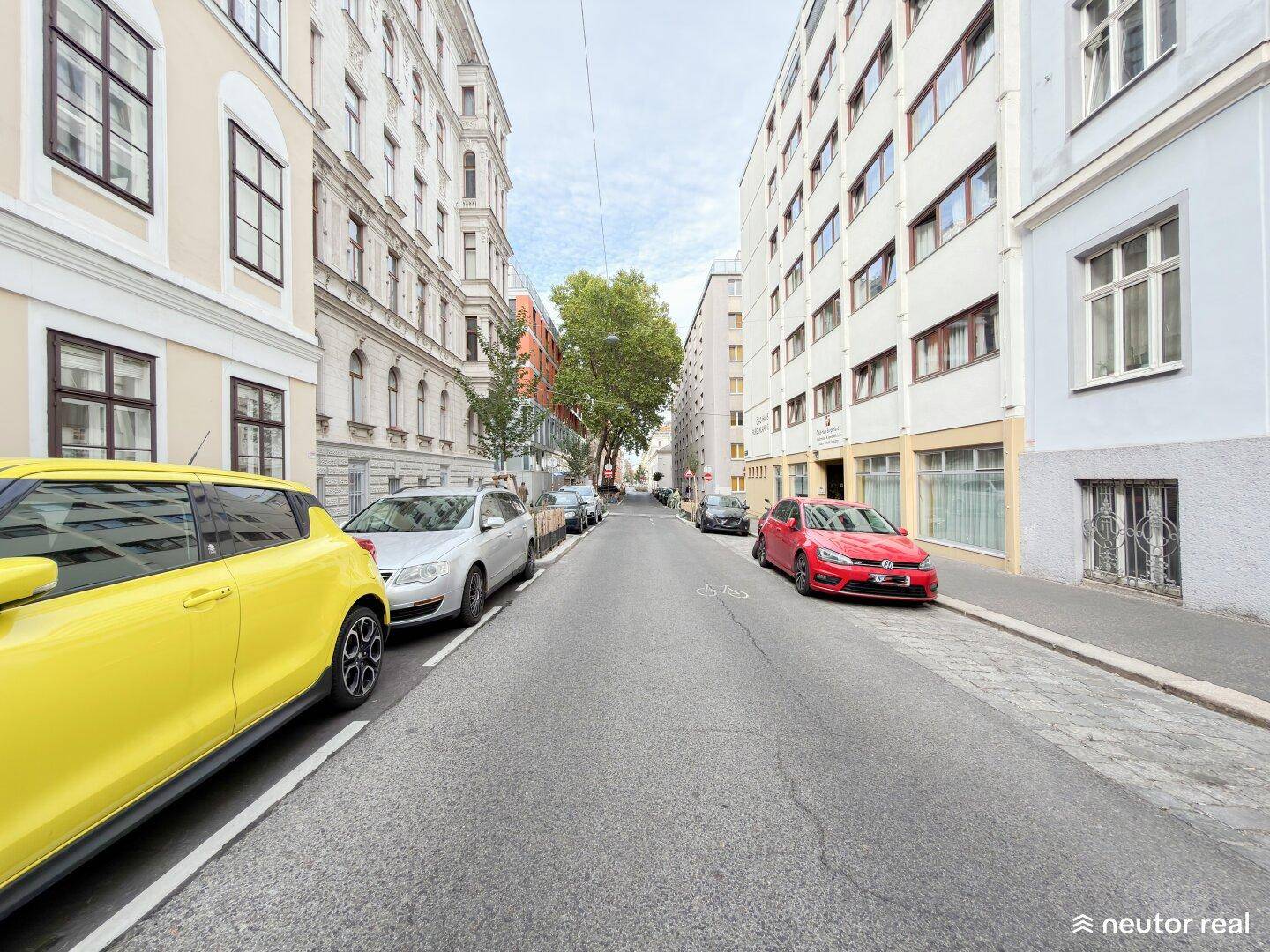 Blick auf eine städtische Straße mit parkenden Autos und hohen Wohngebäuden auf beiden Seiten.
