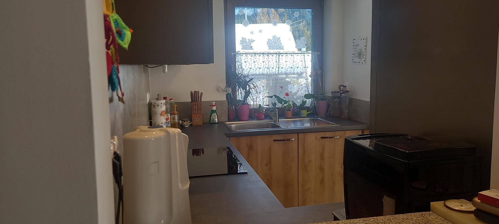 Funktionale Küche mit Spülbecken unter dem Fenster und Arbeitsflächen aus dunklem Material.