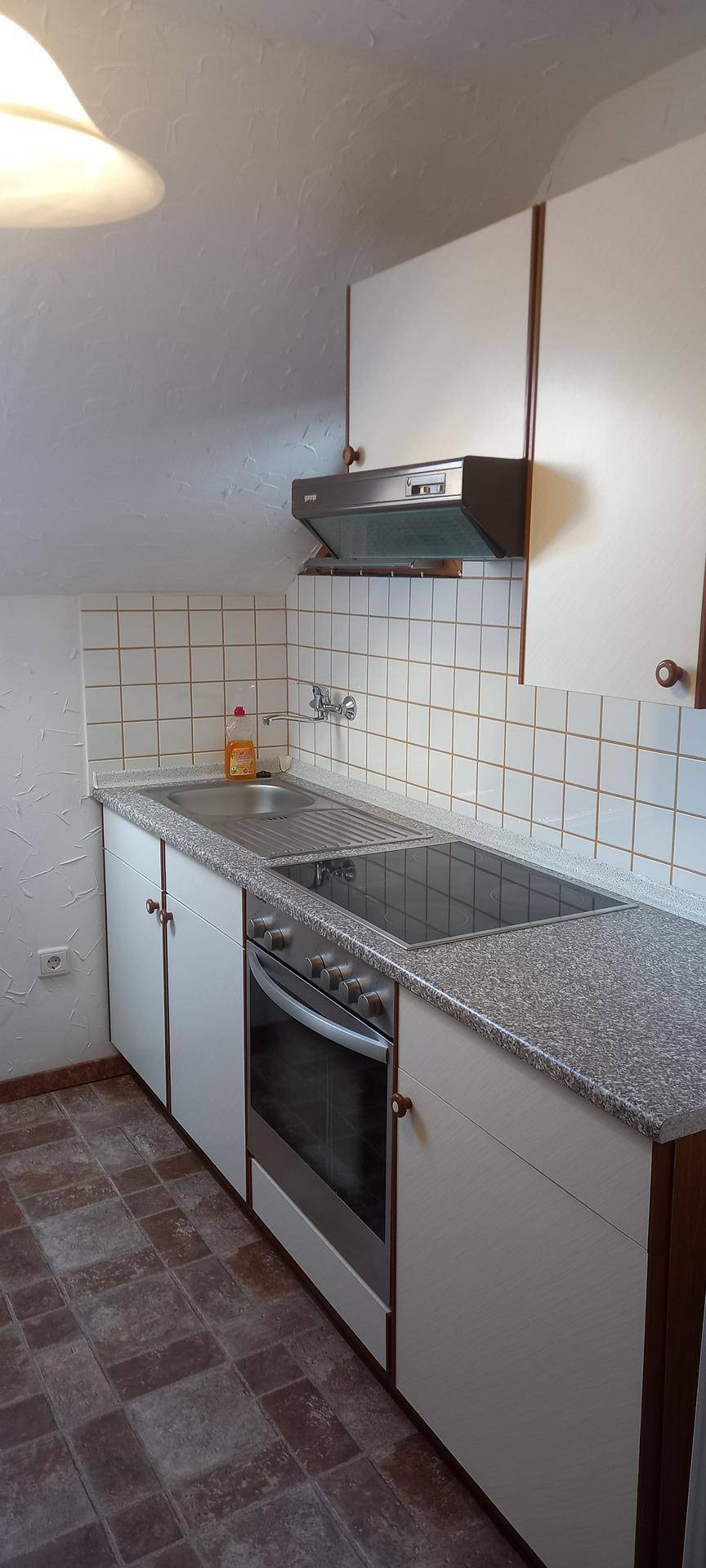 Kleine Küche mit weißen Schränken, Fliesenrückwand und integriertem Kochfeld und Backofen.