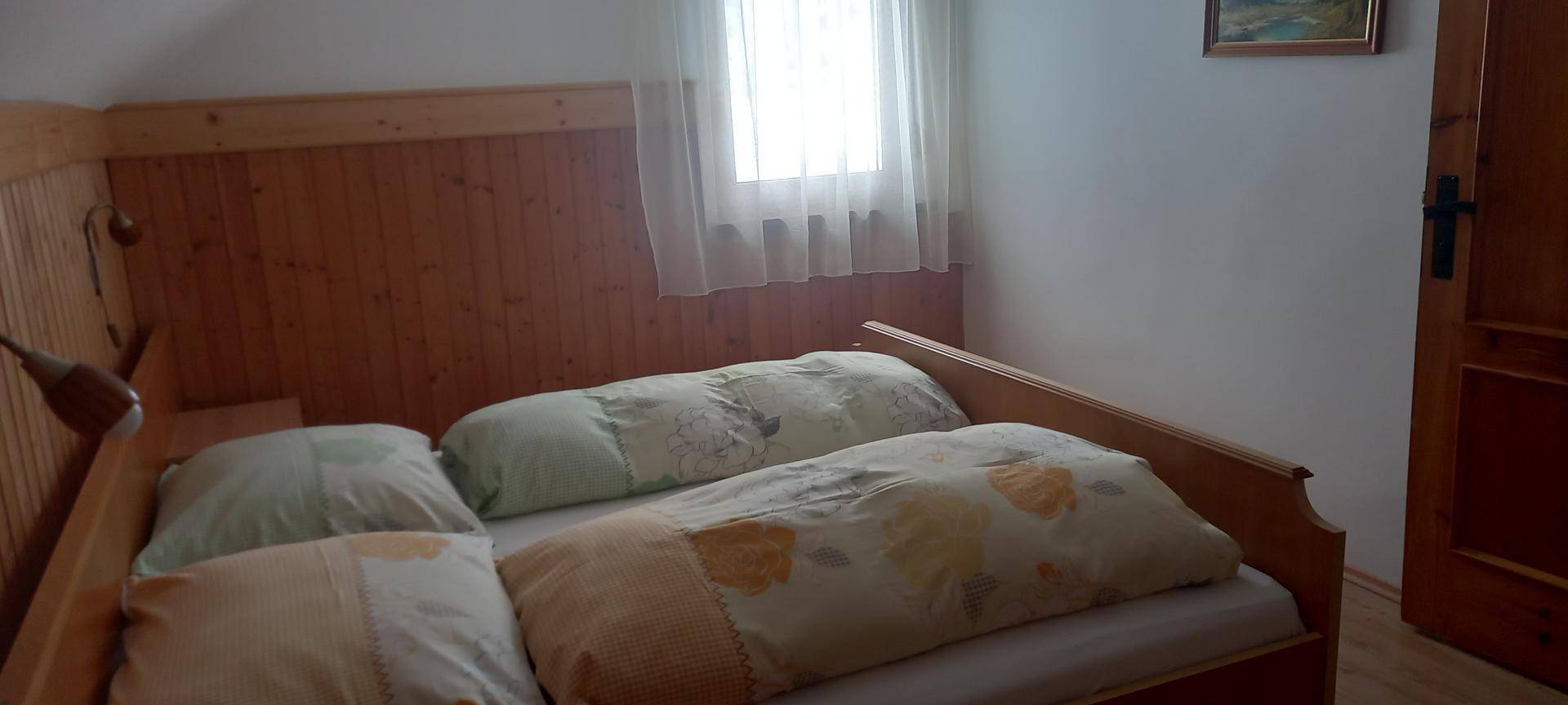 Helles Schlafzimmer mit Holzvertäfelung, Einzelbett und Fenster mit Blick ins Grüne.