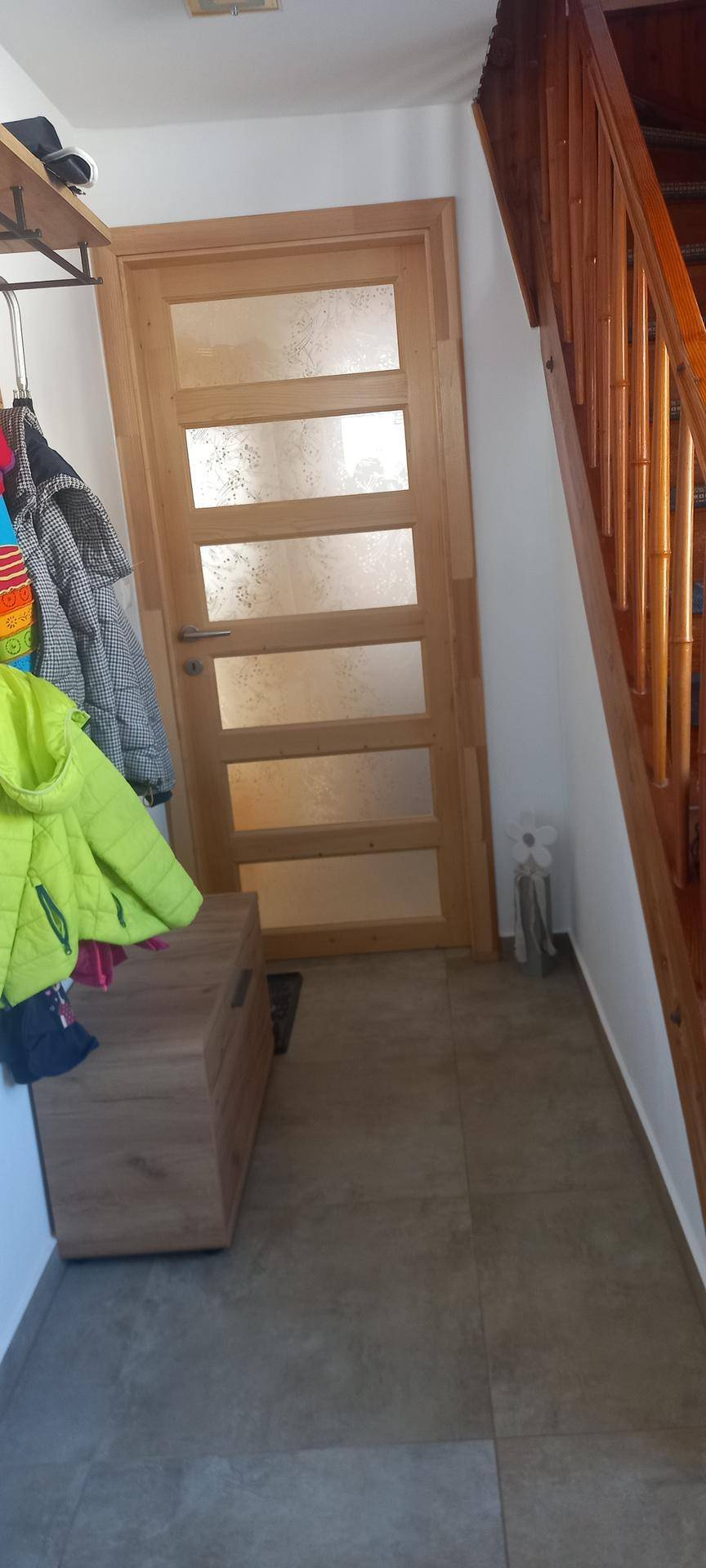 Heller Flur mit Holztreppe und moderner Holztür mit Glaseinsätzen.